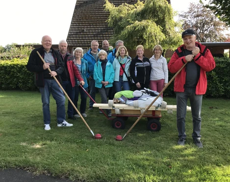 Aus dem Ammerländer Leben Eine Gruppe von elf älteren Menschen posiert lächelnd auf einer grünen Wiese mit einem Bollerwagen und Klootschießen-Stöcken.