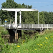 Brücke am Nordloh Kanal Die Brücke am Nordloh Kanal ist eine schlichte, weiße Klappbrücke aus Stahl, die über einen ruhigen, schmalen Kanal im Grünen führt. Sie ist umgeben von einer ländlichen Landschaft mit Gras und vereinzelten Bäumen im Hintergrund.