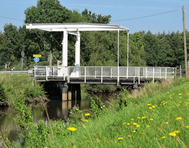 Brücke am Nordloh Kanal Die Brücke am Nordloh Kanal ist eine schlichte, weiße Klappbrücke aus Stahl, die über einen ruhigen, schmalen Kanal im Grünen führt. Sie ist umgeben von einer ländlichen Landschaft mit Gras und vereinzelten Bäumen im Hintergrund.