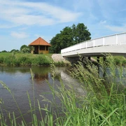 Bokeler Brücke Eine weiße Brücke überspannt das Aper Tief in einer ländlichen Umgebung. Im Hintergrund steht ein Pavillon.