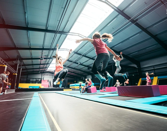 Trampolinpark Abenteuerland Mehrere Personen springen auf parallel angeordneten Trampolinen in einer hellen Halle.
