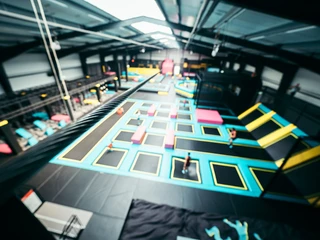 Das Abenteuerland in Bispingen Das Bild zeigt eine große, helle Halle mit verschiedenen Trampolinen in leuchtenden Farben, die zur sportlichen Nutzung angeordnet sind. Bewegung im Hintergrund deutet auf aktive Besucher hin.