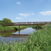Große Süderbäke mit Heeren Wehren Brücke Eine Holzbrücke überspannt die ruhige Große Süderbäke, umgeben von grüner Natur unter blauem Himmel.