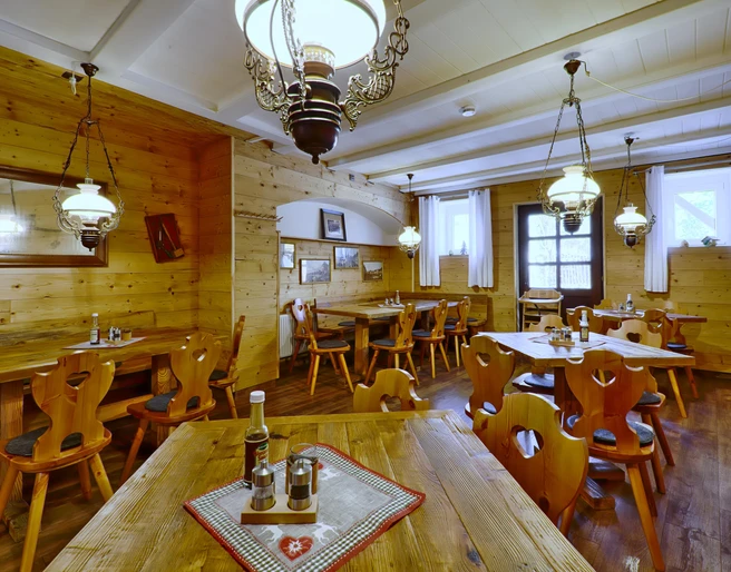 Gemütliches Restaurant mit Holzwänden und -möbeln, dekoriert mit Lampen und Bildern; Tische sind mit Gewürzen und Flaschen gedeckt.