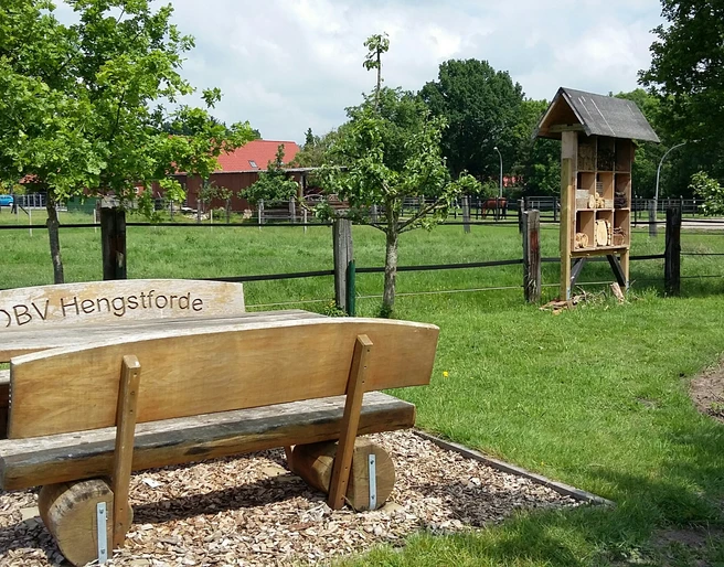 Rastplatz Hengstforde-Apen Ein ruhiger Rastplatz mit einer Holzbänken-Garnitur des OBV Hengstforde, grüner Wiese und Insektenhotel.