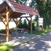 Rastplatz Alter Kirchweg Ein hölzerner Unterstand mit rotem Ziegeldach bietet Schutz, umgeben von Bäumen und neben einem Weg.