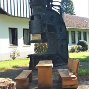 Schmiedehammer am Rastplatz Auf dem Bild ist ein historischer Schmiedehammer zu sehen, der als Rastplatz mit Sitzbänken dient.