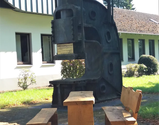 Schmiedehammer am Rastplatz Auf dem Bild ist ein historischer Schmiedehammer zu sehen, der als Rastplatz mit Sitzbänken dient.