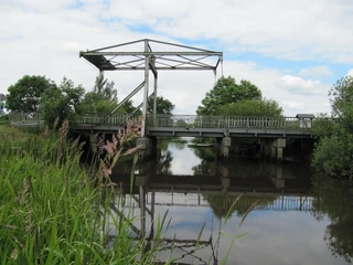 Alte Staaßenbrücke Eine alte, metallene Zugbrücke über einem ruhigen Kanal, umgeben von üppigem Grün.