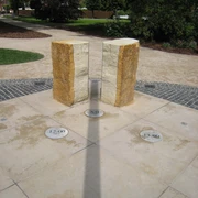 Zwei aufrecht stehende Steinsäulen einer Sonnenuhr werfen einen Schatten auf den darunter liegenden Boden.