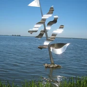 Eine moderne, silberne Skulptur eines Segels mit Wellen steht im klaren Wasser eines Sees.