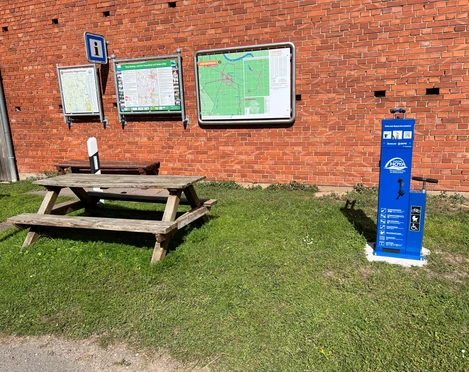 Lufttankstelle Wienbergen Fahrrad-Lufttankstelle neben Picknicktisch vor einer Ziegelwand mit Informationsschildern.