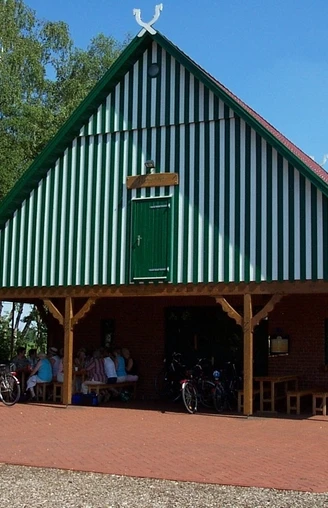 Backsteingebäude mit grünen Fensterläden und Satteldach, umgeben von Fahrrädern und Bäumen.