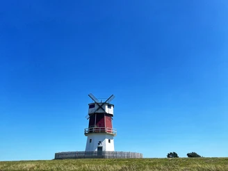 Eine rote Windmühle steht auf einem grünen Hügel unter einem strahlend blauen Himmel.