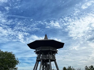 Ein hölzerner Aussichtsturm erhebt sich unter einem blauen Himmel mit verstreuten Wolkenformationen.