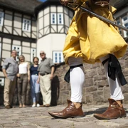 hx_fuehrung_jostziegenhirt_andreashub.jpg Eine Person in historischer Kleidung mit Schwert steht vor einer Gruppe vor Fachwerkhäusern.