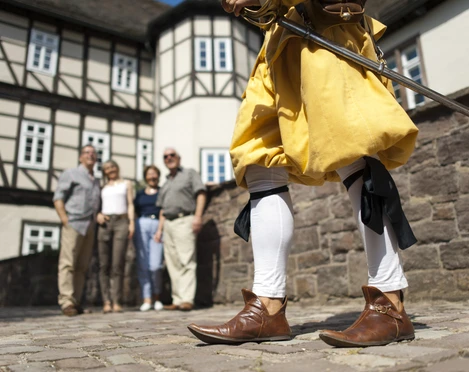 hx_fuehrung_jostziegenhirt_andreashub.jpg Eine Person in historischer Kleidung mit Schwert steht vor einer Gruppe vor Fachwerkhäusern.