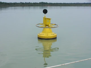 Gelbe Boje im Steinhuder Meer, von Wasser umgeben, trägt ein Schild und reflektiert sich im ruhigen See.
