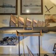 Modell "Steinhuder Hecht" Modell eines Fisches mit Segeln, umgeben von Zeichnungen und nautischen Instrumenten an der Wand.