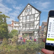Wasserwege-Zimmerhof Handydisplay zeigt Stationsübersicht, Fachwerkhaus mit Terrasse am Wasser