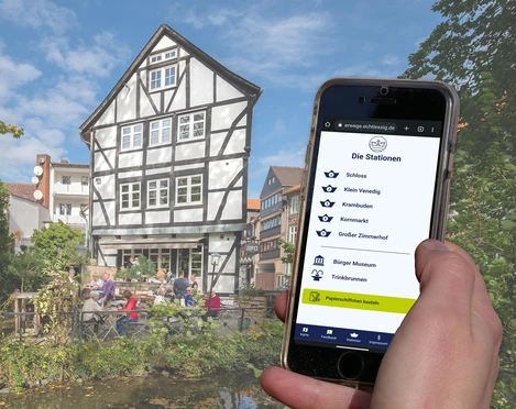 Wasserwege-Zimmerhof Handydisplay zeigt Stationsübersicht, Fachwerkhaus mit Terrasse am Wasser