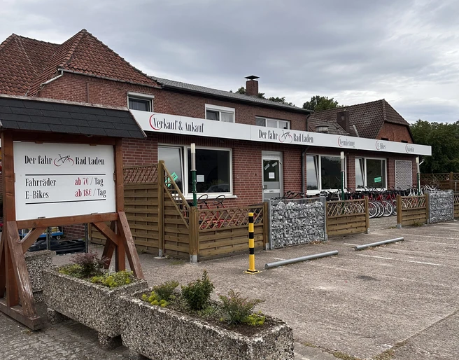Fahrradverleih Mardorf am Steinhuder Meer Fahrradverleihstation mit E-Bikes in einem roten Backsteingebäude vor bewölktem Himmel.