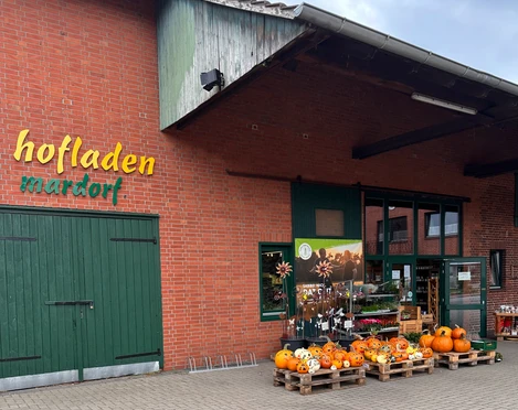 Hofladen Niemeyer Hofladen mit Backsteinfassade und grünem Holztor, dekoriert mit Kürbissen und Blumenschildern.