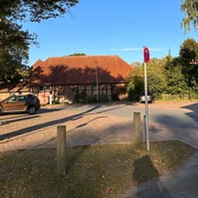 Parkplatz mit Pflastersteinen, umrahmt von Bäumen und einem Gebäude mit rotem Ziegeldach.