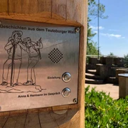Hörstation Anna & Hermann in Hörstel Hörstation im Teutoburger Wald mit Schildern für Audio-Einleitung, umgeben von Bäumen und Natur.
