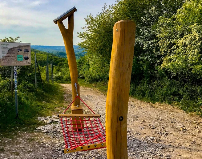Hörstation 05 am Dyckerhoff Steinbruch Hörstation im Dyckerhoff Steinbruch, umgeben von Bäumen, mit Info-Tafel und Seilnetz zum Entspannen.