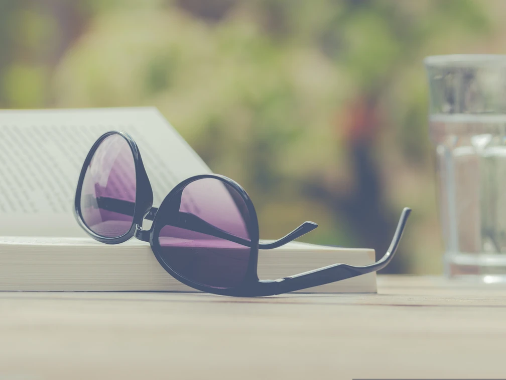 Aufgeschlagene Brille auf einem Buch, daneben ein Glas Wasser auf einem Tisch.Glasses open on a book, next to a glass of water on a table.