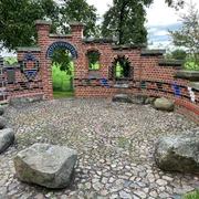 Altenbücken Kreative Backsteinarchitektur mit bunten Fliesen und Natursteinen auf einer runden Pflasterfläche im Grünen.