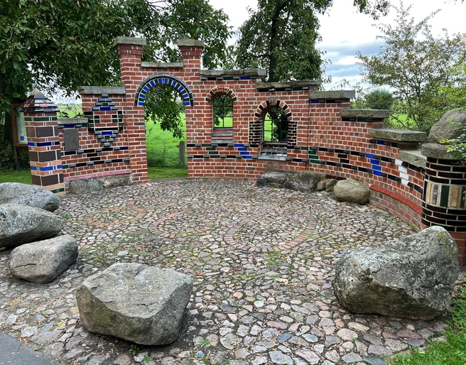 Altenbücken Kreative Backsteinarchitektur mit bunten Fliesen und Natursteinen auf einer runden Pflasterfläche im Grünen.