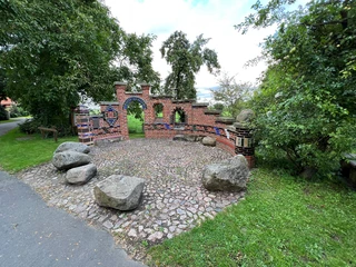 Altenbücken Roter Backsteinbogen mit blauen Details und hölzernen Bänken in einer grünen Parkumgebung.
