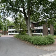 Rotes Backsteingebäude des Rathauses Kirchlinteln umgeben von grünen Bäumen und Gehwegen.