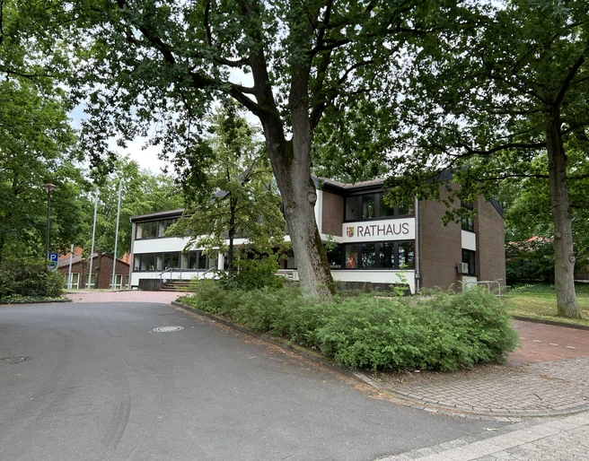 Rotes Backsteingebäude des Rathauses Kirchlinteln umgeben von grünen Bäumen und Gehwegen.