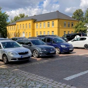 Parkplatz_Rathaus1_22082023_PetraRoemer.jpg Parkplatz mit Autos. Im Hintergrund steht das gelbe Rathaus