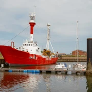 Das rot-weiße Feuerschiff liegt im Borkumer Hafen. Der Himmel ist grau bewölkt.The red and white fire ship is in the harbor of Borkum. The sky is gray and overcast.