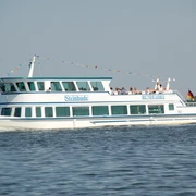 FGS Steinhude Ein weiß-blaues Fahrgastschiff namens Steinhude gleitet mit Menschen an Bord über einen See bei Sonnenschein.