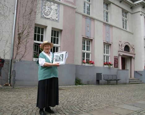 "Bürgerin Gesine" vor der Sparkasse Achim Gesine, eine ältere Frau in traditioneller Kleidung, steht lächelnd vor der Sparkasse Achim.