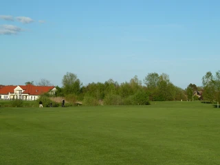 Golfplatz Achim Weitläufiger Golfplatz mit gepflegtem Grün, eingerahmt von Bäumen und einem Gebäude mit rotem Dach.