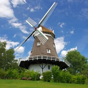 Die Achimer Windmühle steht unter blauem Himmel, umgeben von Bäumen.