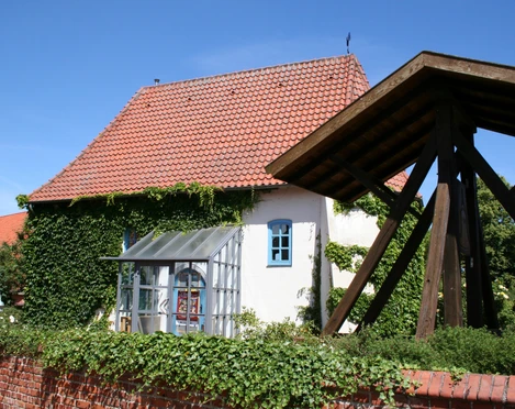 Kulturzentrum Alte Kapelle Haßbergen Das Bild zeigt die Alte Kapelle Haßbergen mit ihrem rot gedeckten Dach und von Efeu bewachsenen Wänden.