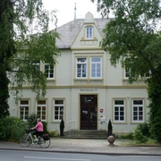 Altes Rathaus Zweistöckiges Gebäude mit gelber Fassade, üppiges Grün, vorbei radelnde Person auf der Straße.