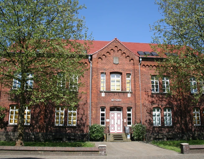 Amtsgericht Achim Backsteinfassade des Amtsgerichts Achim, flankiert von Bäumen unter blauem Himmel, Eingang mittig.