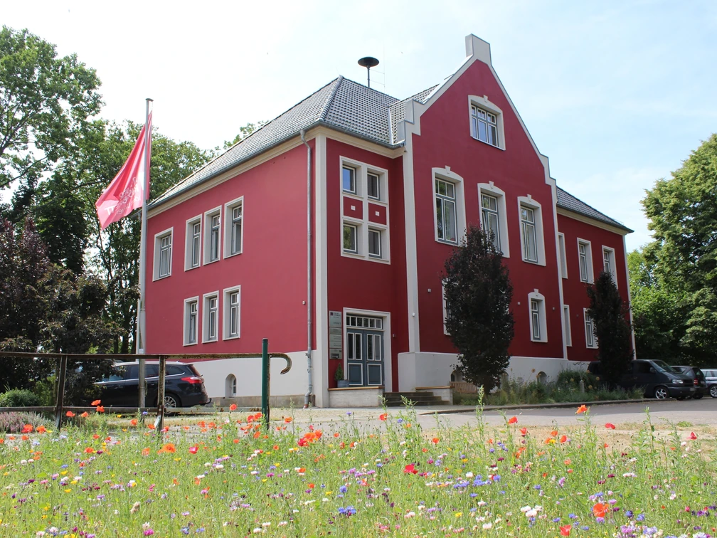 Amtshof 1 Bruchhausen-Vilsen Amtshof 1 in Bruchhausen-Vilsen, ein rotes Gebäude mit weißen Fensterrahmen und Blumenwiese davor.