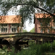 Aue-Brücke Steyerberg Die Aue-Brücke in Steyerberg, umgeben von Bäumen, verbindet historische Backsteingebäude über einen Fluss.