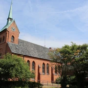 Kirche Bruchhausen Backsteinkirche mit Spitzdach und Turm im Dorf Bruchhausen; von Bäumen umgeben, blauer Himmel.