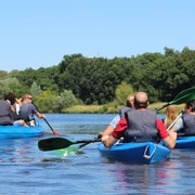 Kanutour Mittelweser Eine Gruppe von Menschen in blauen Kanus paddelt über einen ruhigen Fluss, umgeben von grünen Bäumen.
