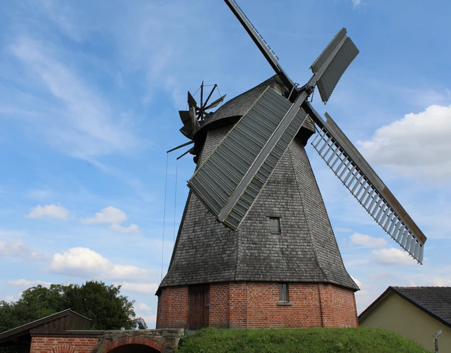 Büschings Mühle Petershagen Historische Windmühle mit Backsteinsockel und Holzverkleidung vor blauem Himmel in Petershagen.
